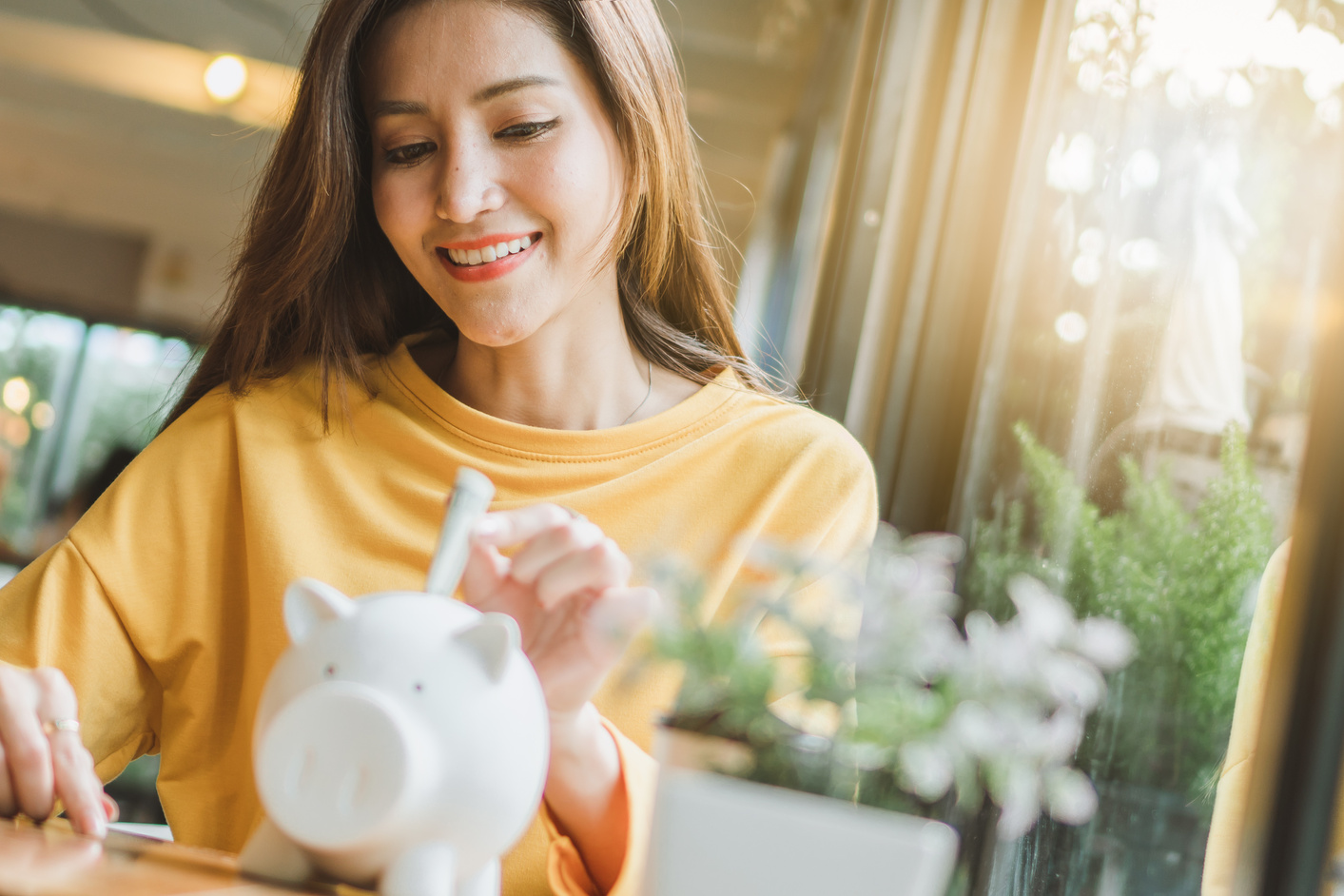 Asian woman saving money and dropping coin to piggy